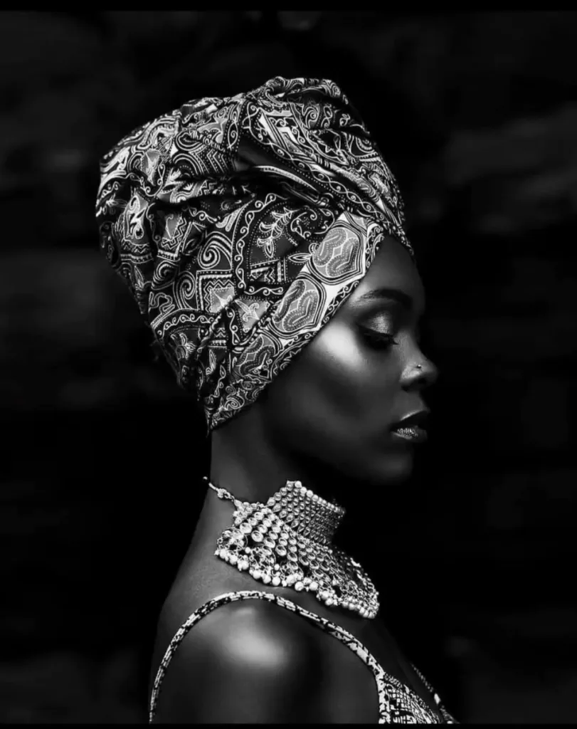 Black-and-white profile portrait of Jahnelle wearing a patterned headwrap and ornate necklace
